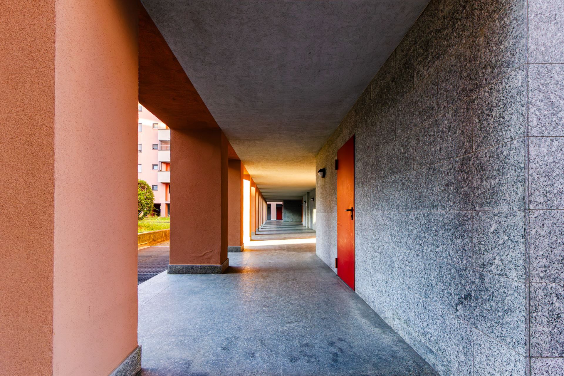 Un corridoio con pavimento piastrellato, soffitto in cemento e pareti dalla finitura strutturata.
