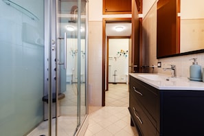 Un baño moderno con cabina de ducha de vidrio, tocador con lavamanos y un espejo grande.