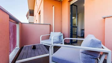 Un balcone con due sedie di metallo bianco e un tavolo di legno, una porta rossa e un muro bianco.