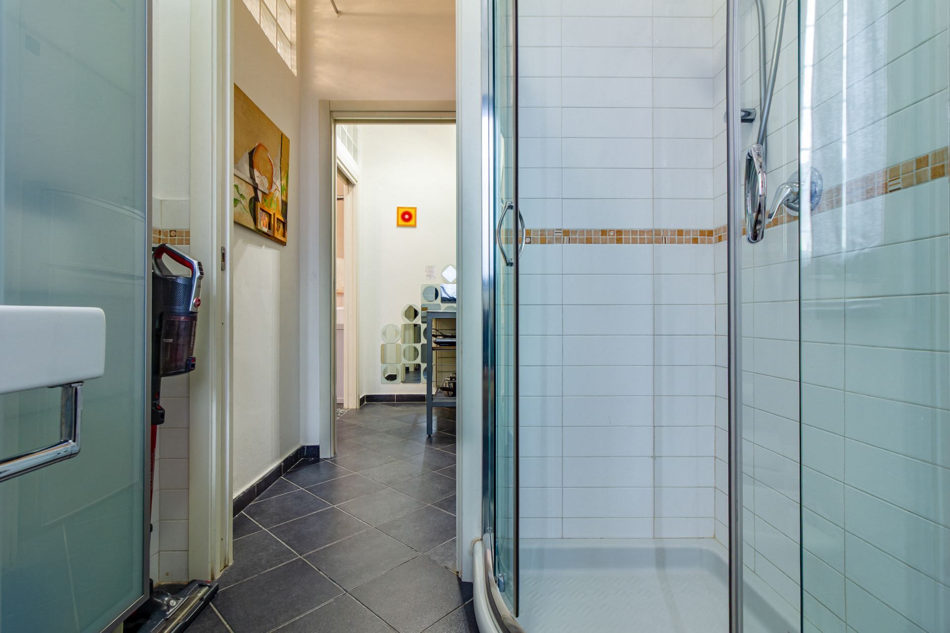 Un corridoio che conduce a un bagno con cabina doccia in vetro e pareti rivestite di piastrelle.