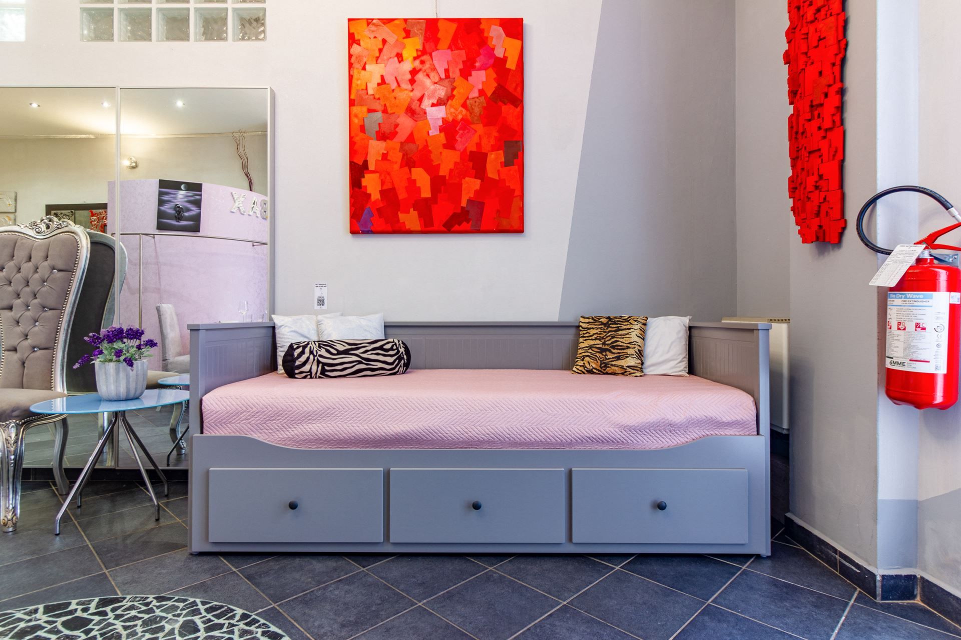 Een moderne hotelkamer met een bed, een bureau en een stoel. Aan de muur hangt een rode brandblusser.