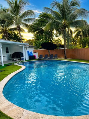 A swimming pool with a sun deck, lounge chairs, and a covered area with umbrellas. - Luxury 5BR Heated Pool, Game Room, Sandy Beach Area & Basketball (Miami)