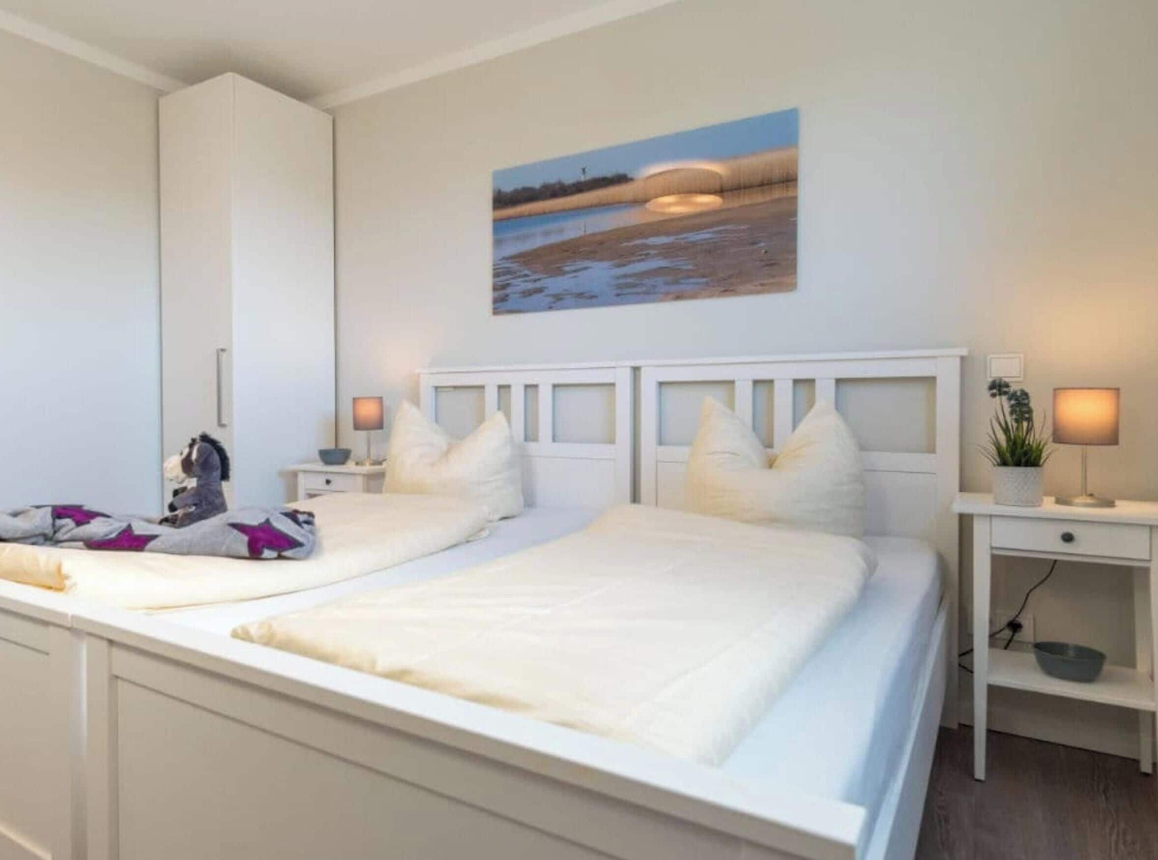 Ein Schlafzimmer mit zwei Betten, einem Nachttisch mit Lampe, einem Wandbild und einem kleinen Schreibtisch mit Pflanze.