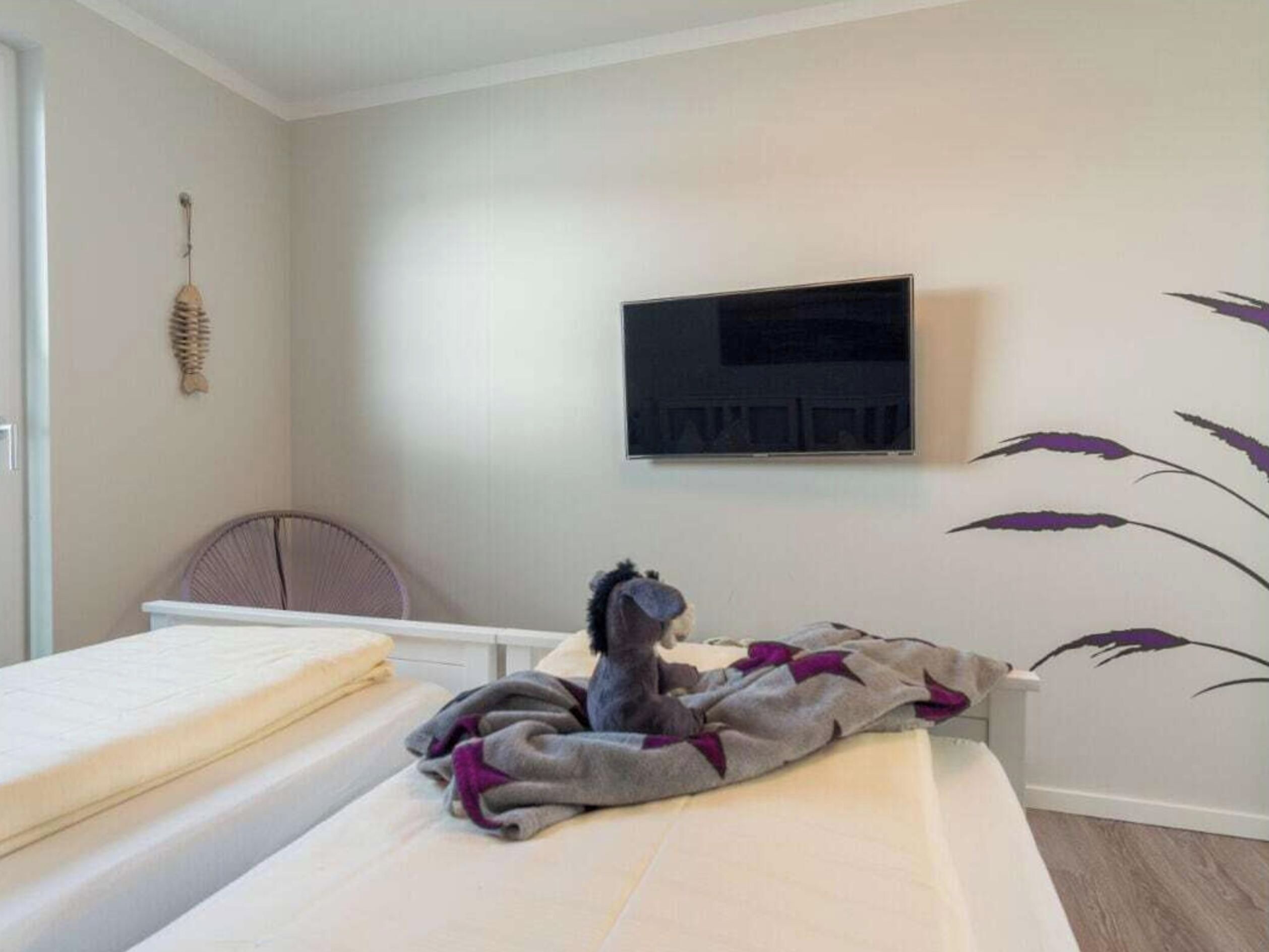 Une chambre à coucher avec un lit, un téléviseur fixé au mur et une chaise.