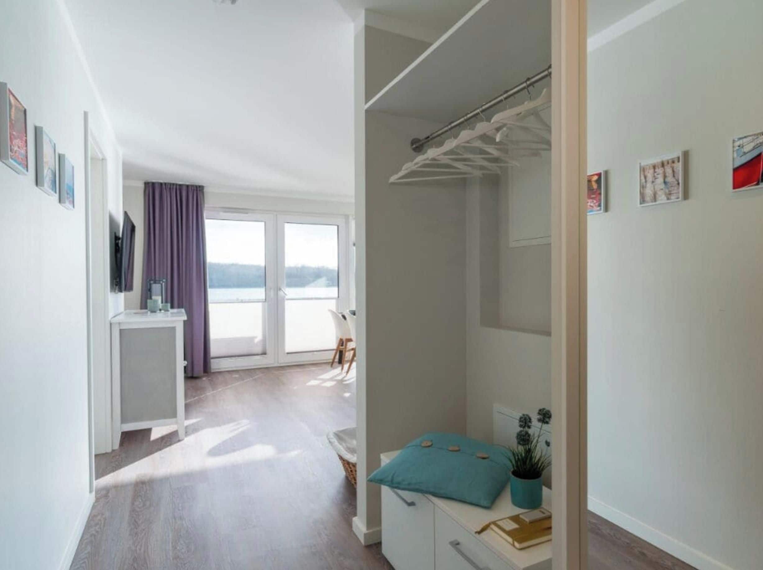 Quarto moderno com grande porta de vidro deslizante para uma varanda, guarda-roupa branco e pequena mesa com planta.