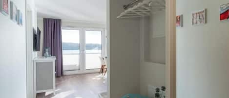 Et moderne værelse med en stor skydedør til en balkon, et hvidt skab og et lille skrivebord med en plante.