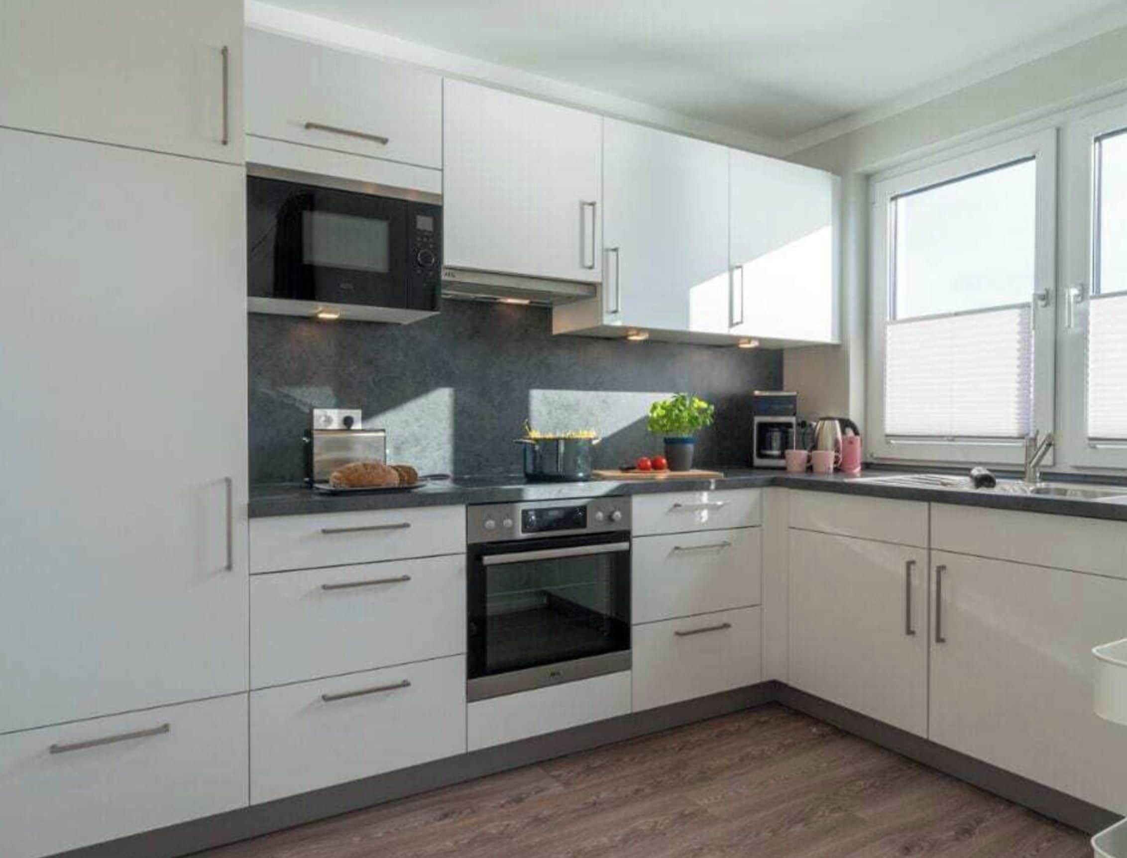 Una cocina moderna con armarios blancos, horno empotrado, microondas y ventana que proporciona luz natural.
