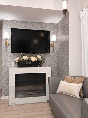 A modern living room with a flat-screen TV mounted on a textured wall, a fireplace with a flower arrangement, and a grey sofa with a cushion. - CONDESA Two Bedroom, Pool, Gym Security 24/7 for group of 6. (Ciudad de México)