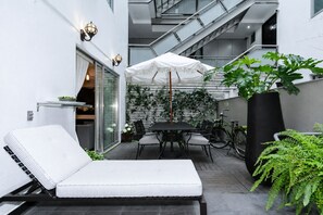 Un patio moderno al aire libre con una silla de salón, una mesa de comedor y una sombrilla.