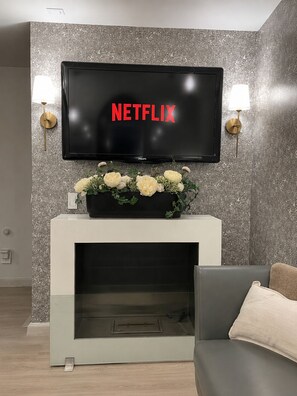 Ein modernes Wohnzimmer mit einem flachbildfernseher an einer strukturierten Wand, einem Kamin und einer Blumenkomposition auf einem Sofa.
