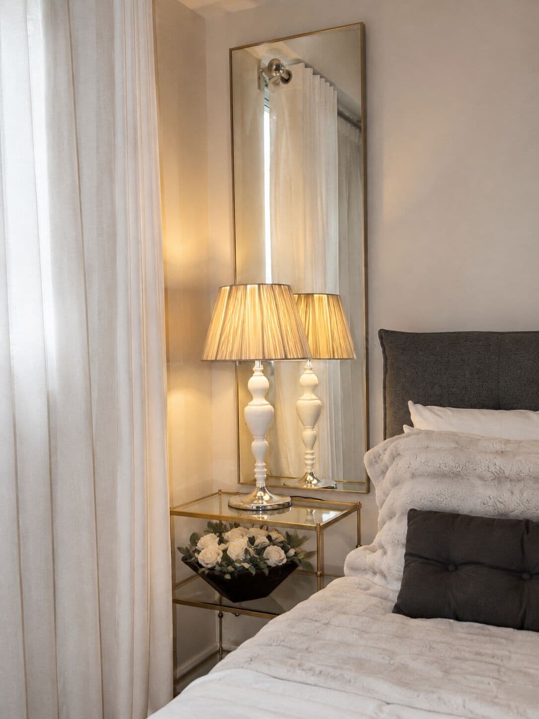 A neatly arranged bedroom with a bed, bedside table, lamp, and a mirror.
