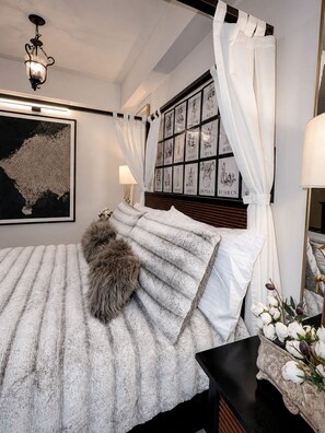 Un dormitorio con una cama grande, dosel, una obra de arte enmarcada y una mesita de noche con lámpara.