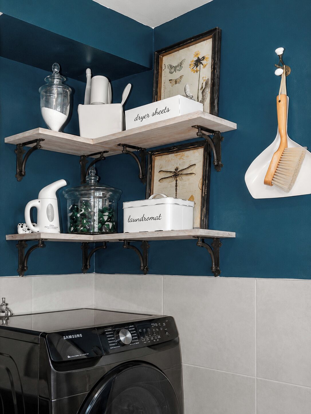 A laundry area with a Samsung washing machine, shelves with labeled containers, and a decorative wall piece.