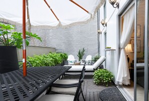 Un espacio de estar al aire libre techado con una mesa y sillas, rodeado de plantas en macetas y un toldo blanco.