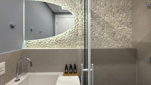 A modern bathroom with a bathtub, a glass shower enclosure, and a mirror reflecting a textured wall. - Vrbo Property (São Paulo)