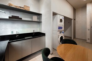 A modern kitchen with a built-in washing machine and a dining area with a wooden table and chairs. - Studio Le Jardin Cyrela · Pinheiros · Oscar Freire Metro Station (São Paulo)