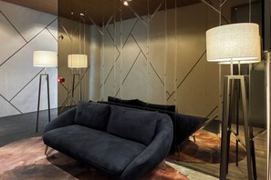 Ein modernes Interieur mit einem dunklen Sofa, Stehlampen und geometrischen Wandmustern.