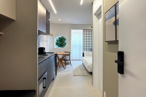Cuina moderna amb zona de menjador, una finestra gran i un llit a l'habitació veïna.