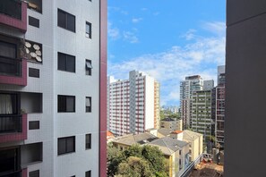 Un edifici alt amb nombroses finestres i balcons, envoltat d'altres edificis i arbres.