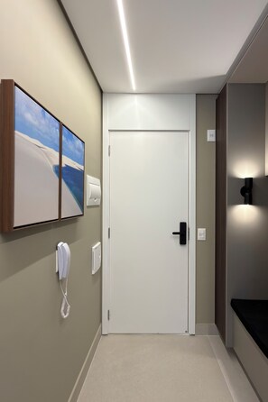 A hotel hallway with a white door, a wall-mounted phone, a towel dispenser, and a framed picture. - Studio Le Jardin Cyrela · Pinheiros · Oscar Freire Metro Station (São Paulo)