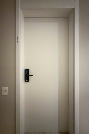 Eine Tür mit einem modernen elektronischen Schloss und einem Lichtschalter an der Wand.