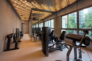 Ein Fitnessstudio mit Trainingsgeräten, großen Fenstern und einer gemusterten Decke.