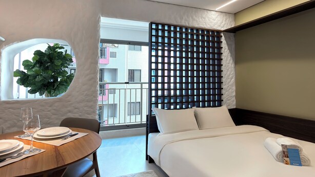 A hotel room with a bed, a dining table with plates and cutlery, a potted plant, and a view of the outside. - Vrbo Property (São Paulo)