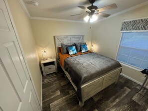 Ein Schlafzimmer mit Bett, Nachttisch, Deckenventilator und Fenster mit Jalousien.