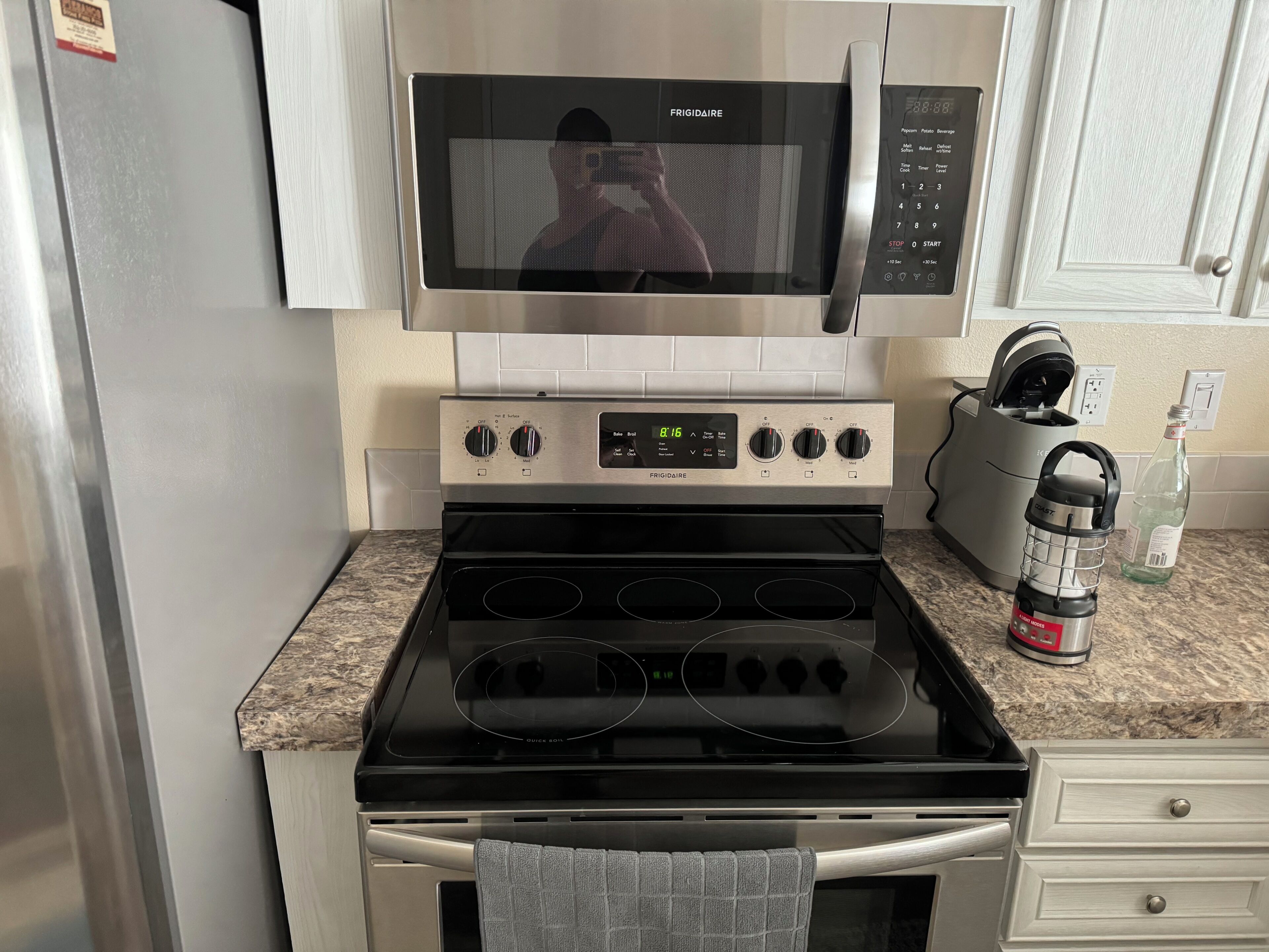 Cuina amb microones d'acer inoxidable, panell de control digital del forn, una tetera i una ampolla d'aigua sobre el taulell.
