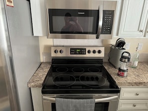 A kitchen with a stainless steel microwave, a digital oven control panel, a kettle, and a water bottle on the counter.