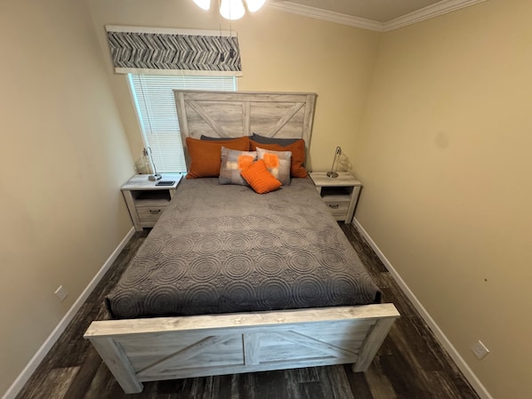 A bedroom with a bed, nightstands, a lamp, and a window with blinds.