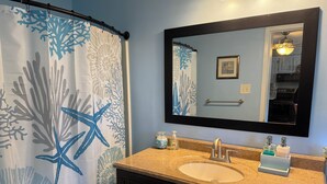 A bathroom with a shower curtain featuring a blue starfish and coral pattern, a sink with a beige countertop, a mirror above the sink, and a door with a handle. - 2-bedroom condo in welcoming Plaistow close to beaches, mountains, and Boston (Plaistow)