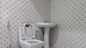 Et badeværelse med toilet og et håndvaskestel foran en flisebelagt væg.