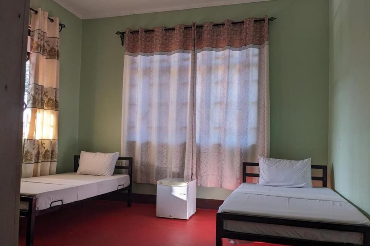 A room with two single beds, a small bedside table, and a window with curtains.