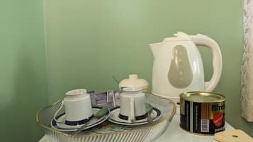 A kitchen counter with a coffee maker, a kettle, a can of food, and a cutting board.