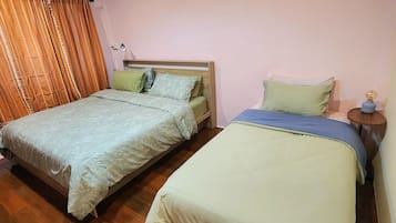 Ein Zimmer mit zwei Betten, Holzboden, einem kleinen Tisch mit Lampe und einem Vorhang.