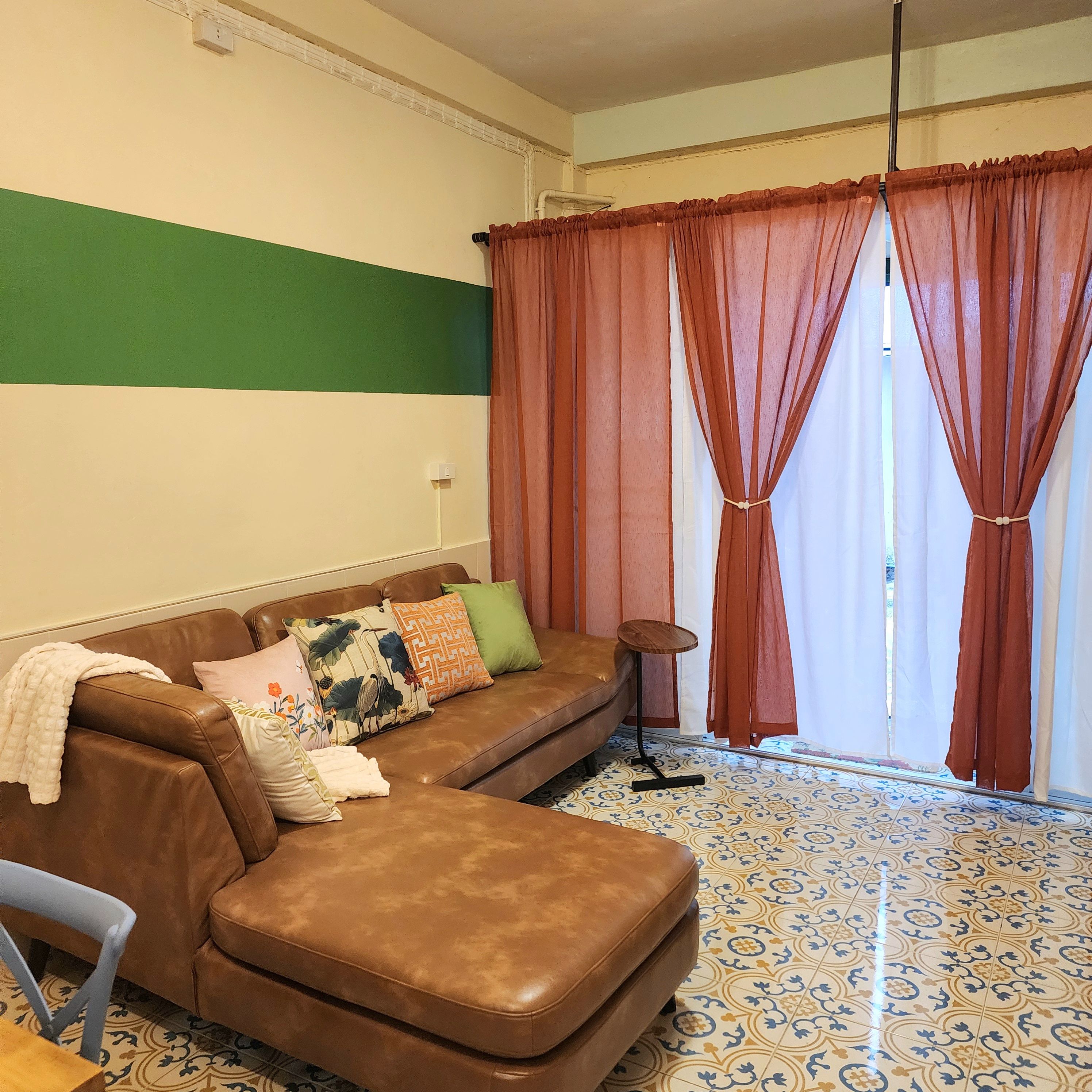 A living room with a brown leather sofa, patterned cushions, a small round table, and a floor with patterned tiles.