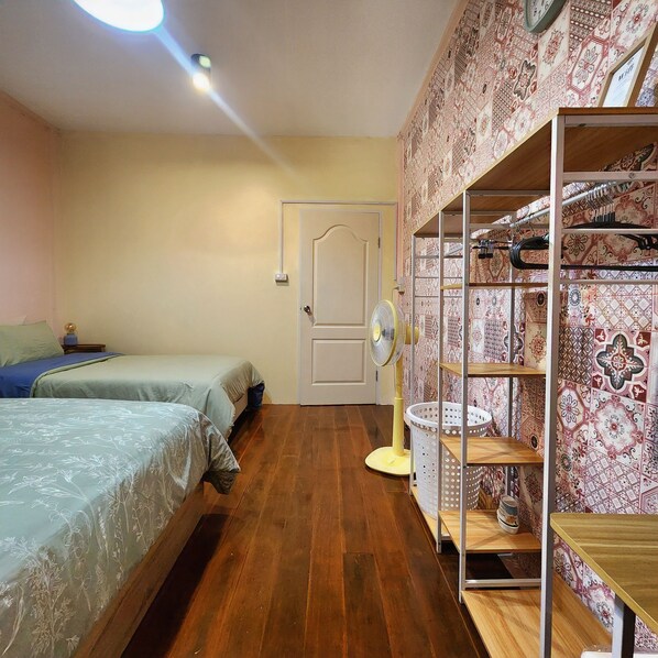 Une chambre avec deux lits, un ventilateur, une porte et un mur décoré de motifs.