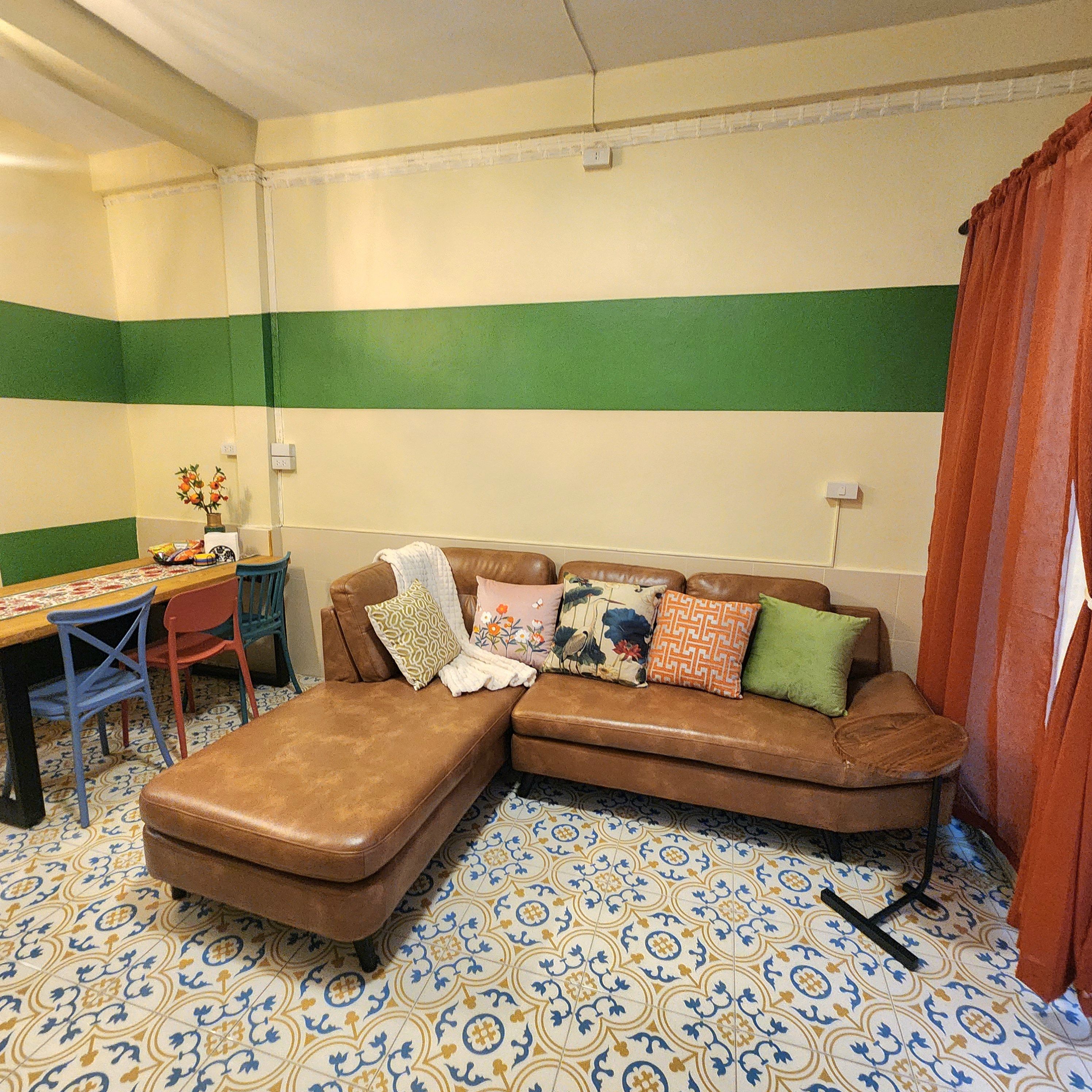 A room with a brown leather sofa, a patterned floor, a dining table with chairs, and a green and white striped wall.