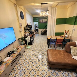 A living room with a television, a sofa, a dining table with chairs, a fan, and a staircase leading to an upper level. - 3BR Local Bangkok Stay [10 Min Walk to BTS & Sathorn Pier ] • Easy City Access (Sathon)