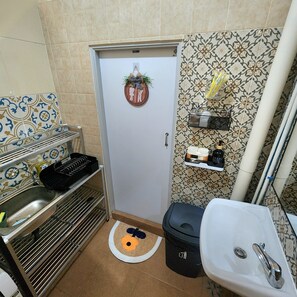 Une petite salle de bain comprenant un lavabo, des toilettes et une petite étagère où sont rangés les articles de toilette.