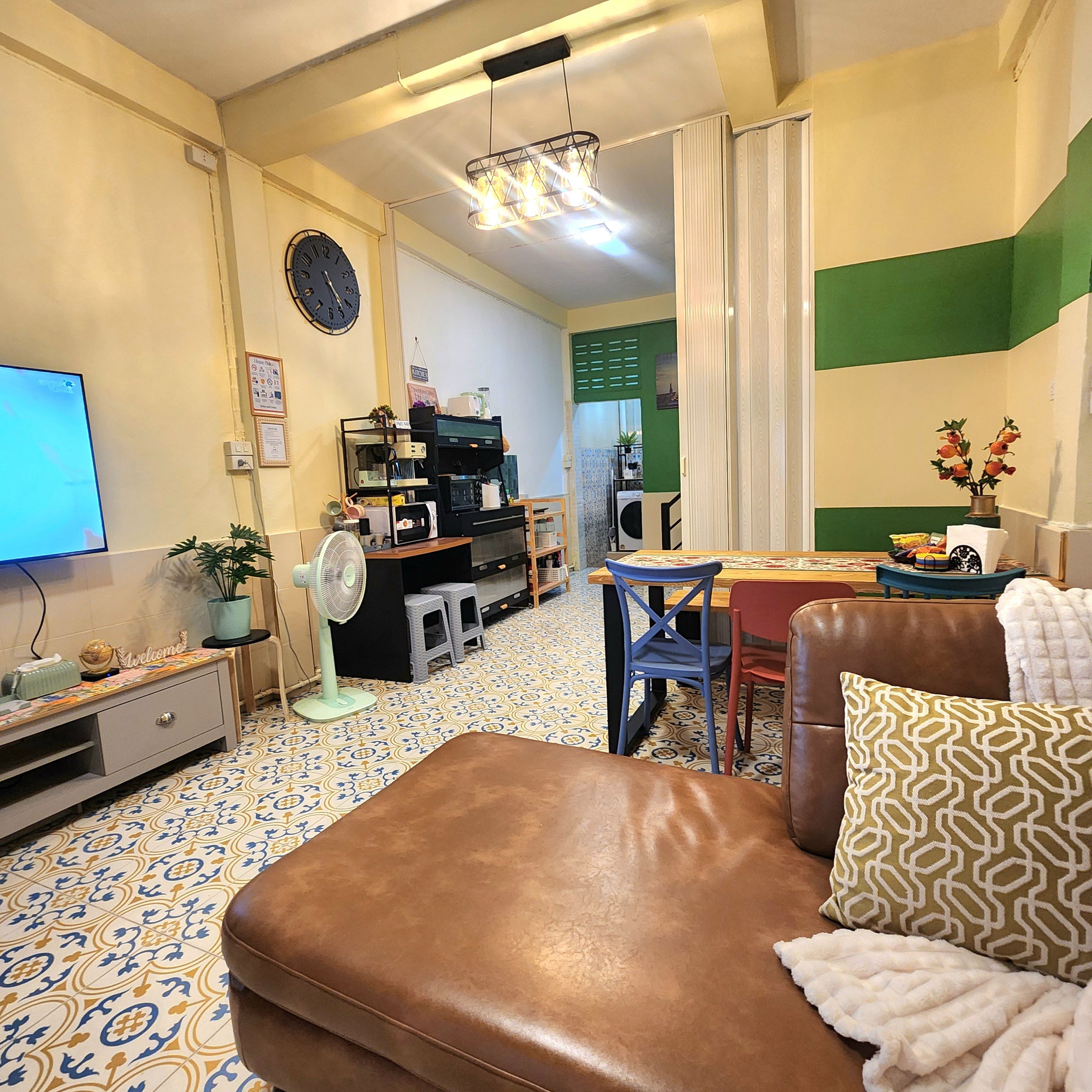 Ein Wohnzimmer mit braunem Ledersofa, Fernseher, Ventilator und einer Kaffeemaschine.