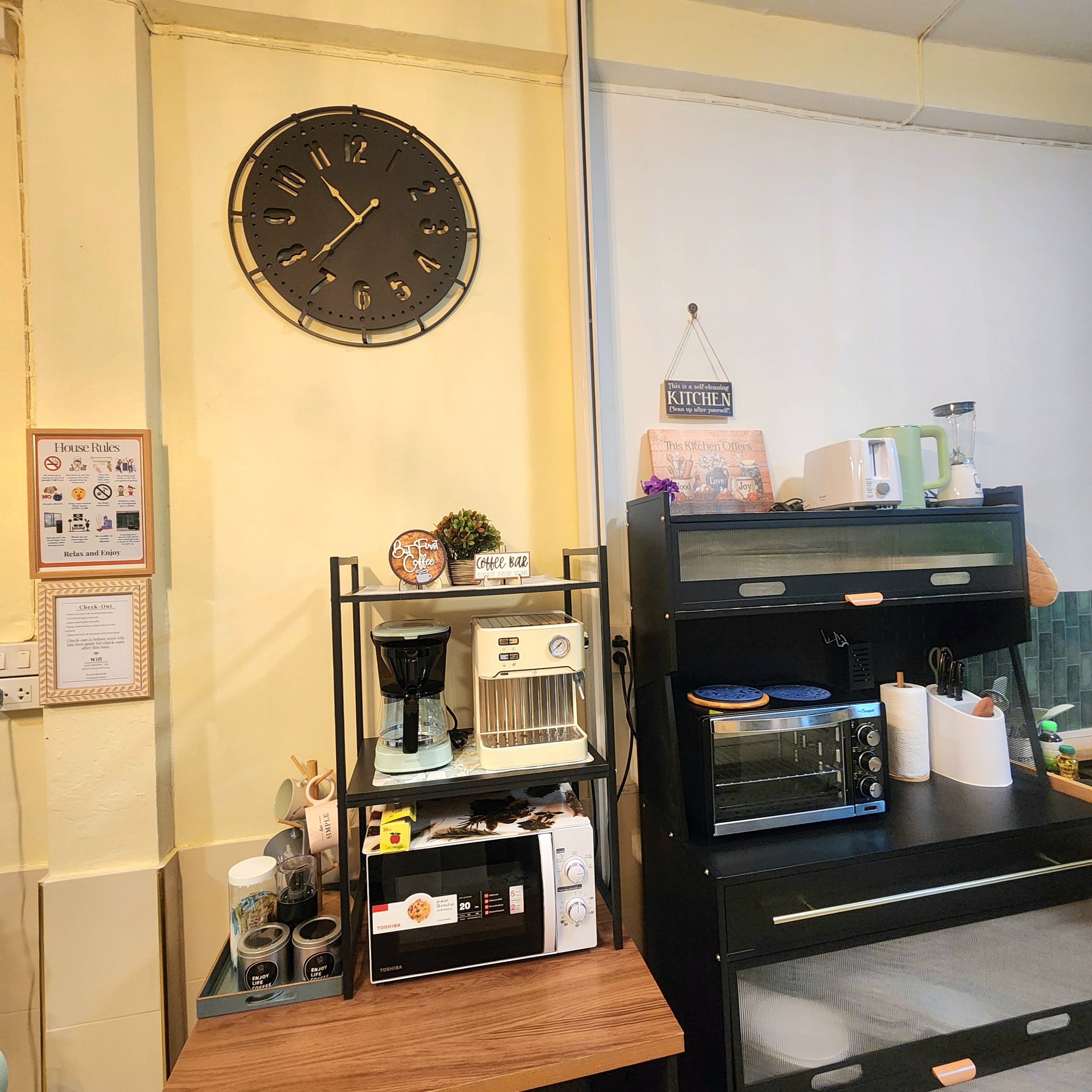 A kitchen area with a clock, coffee machines, and a sign that reads 'This is a self-cleaning kitchen.'