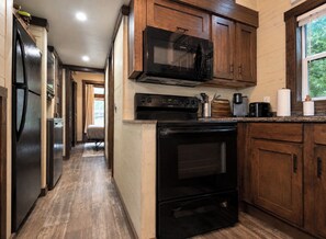 A kitchen with wooden cabinets, a black microwave, a stove, and a refrigerator.