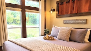 Ein Schlafzimmer mit einem großen Bett, Blick ins Freie, einer Wandleuchte und einem motivierenden Zitat.
