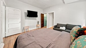 Un dormitorio con una cama grande, un televisor en la pared, un sofá y una mesita.
