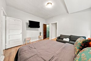 Ett sovrum med en stor säng, en tv på väggen, en soffa och ett litet bord.