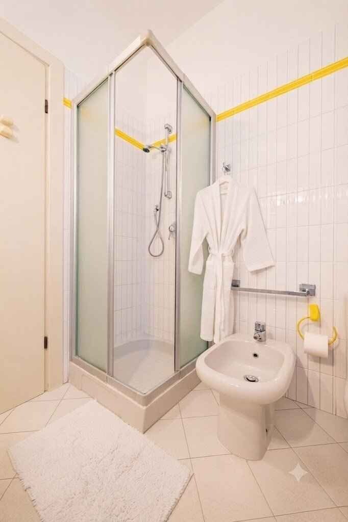 Ein Badezimmer mit einer Duschkabine, einem Bidet und einem weißen Bademantel, der an der Wand hängt.