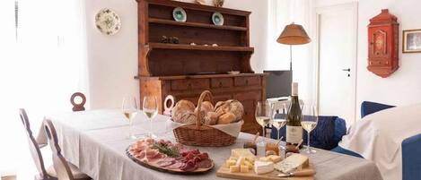 Una mesa de comedor dispuesta con pan, queso y embutidos, un aparador de madera con platos decorativos y una lámpara.