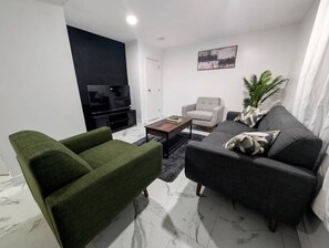 A modern living room with a sofa, armchair, and a flat-screen TV.